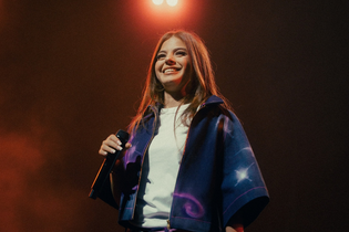Die Künstlerin Zah1de steht auf der Bühne und hält ein Mikrofon in der Hand. Im Hintergrund leuchtet ein Scheinwerfer. | © William Krause
