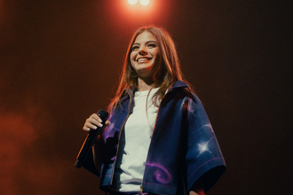Die Künstlerin Zah1de steht auf der Bühne und hält ein Mikrofon in der Hand. Im Hintergrund leuchtet ein Scheinwerfer. | © William Krause