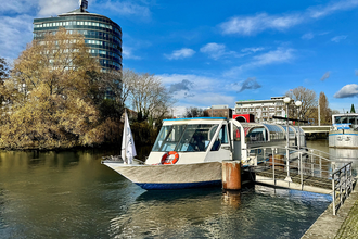 Das Bild zeigt ein Ausflugsboot an der Anlegerstelle "Marrahaus". Ein hohes, modernes Gebäude und Bäume sind im Hintergrund zu sehen. Der Himmel strahlt blau, fast wolkenlos. Die Stimmung ist friedlich und einladend.
