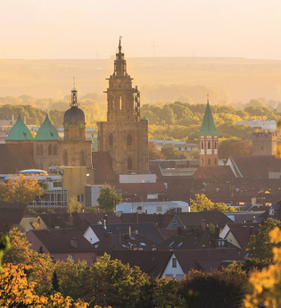 das Bild zeigt die Stadtansicht von Heilbronn mit Kilianskirche, Hafenmarktturm, Deutschhof im warmen Abendlicht umrahmt von Büschen und Bäumen | © Heilbronn Marketing GmbH