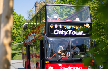 Roter Doppeldeckerbus mit offenem Dach aufgenommen von schräg links vorne. Die Sonne scheint und der Bus ist von grünen Bäumen umgeben | © Heilbronn Marketing GmbH