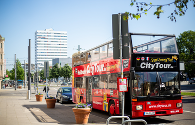 Der rote Doppeldeckerbus steht mit offenem Verdeck an der Haltestelle BW Bank. Im Hintergrund ist das weiße Shoppinghaus - Hochaus zu erkennen | © Heilbronn Marketing GmbH