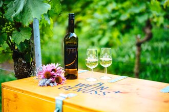Weinflasche und zwei Weingläser stehen auf einer Holzkiste mit der Aufschrift WEIN GENUSS+ | © Biohof Döbler