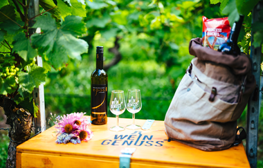 Eine Weinflasche, zwei Weingkläser und eine Rucksack gefüllt mit Snacks stehen auf einer Holzkiste | © Biohof Döbler