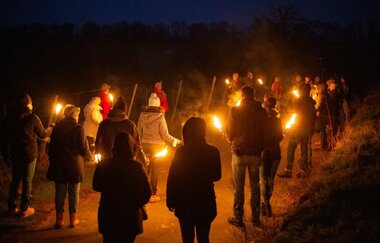 Das Bild zeigt eine Gruppe Menschen, die locker im Kreis stehen und nur die Fackeln in den Händen erhellen die Nacht.