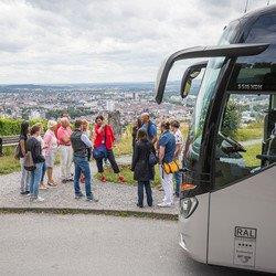 Aussichtspunkt auf dem Wartberg mit Blick auf Heilbronn. Eine Gruppe Teilnehmer steht um eine Stadtführerin herum und bekommt etwas erklärt.  Am rechten Bildrand ist das Fahrerhaus des Busses  ersichtlich
