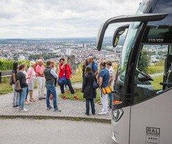 Aussichtspunkt auf dem Wartberg mit Blick auf Heilbronn. Eine Gruppe Teilnehmer steht um eine Stadtführerin herum und bekommt etwas erklärt.  Am rechten Bildrand ist das Fahrerhaus des Busses  ersichtlich