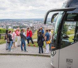 Aussichtspunkt auf dem Wartberg mit Blick auf Heilbronn. Eine Gruppe Teilnehmer steht um eine Stadtführerin herum und bekommt etwas erklärt.  Am rechten Bildrand ist das Fahrerhaus des Busses  ersichtlich