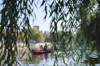 Das Bild wurde zwischen den hängenden Blättern einer Trauerweide aufgenommen. Zu erkennen sind zwei Personen in einem Kanu auf dem Fluss. Im Hintergrund erkennt man einen Turm aus Naturstein | © Heilbronn Marketing GmbH