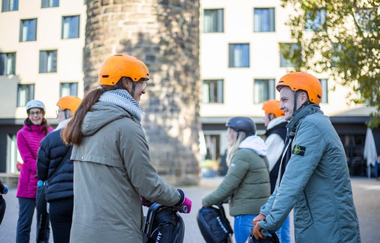 Auf dem Bild sieht man eine Gruppe von Personen auf dem Segway vor dem Bollwerksturm. Die Stimmung scheint gut. Eine Frau im Hintergrund lacht.