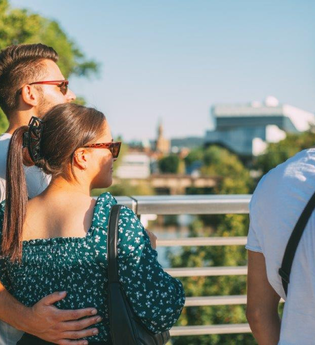 drei Personen stehen vor einem Geländer und schauen in die Ferne . Im Hintergrund ist verschwommen ein weißes Gebäude erkennbar