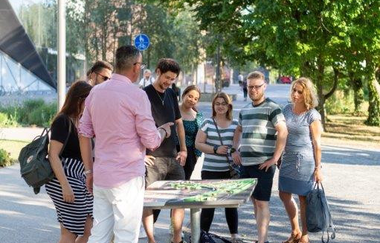 Eine Gruppe steht um eine Bildtafel, die horizontal ausgerichtet ist.