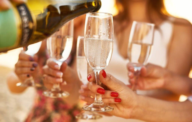 Vier Frauenhände mit gefülltem Sektglas in der Hand . Ein Glas wird gerade mit einer Flasche befüllt