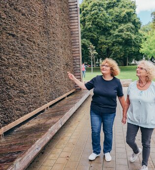Zwei Besucherinnen stehen vor dem Gradierwerk in Bad Rappenau. Eine der beiden zeigt auf das Gradierwerk. | © Stadt Bad Rappenau, Chris Frumolt