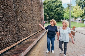 Zwei Besucherinnen stehen vor dem Gradierwerk in Bad Rappenau. Eine der beiden zeigt auf das Gradierwerk. | © Stadt Bad Rappenau, Chris Frumolt