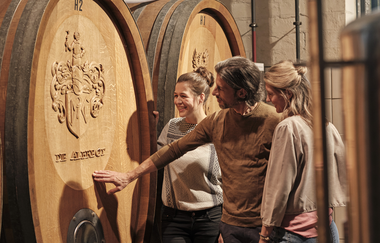 zwei Frauen und ein Mann stehen vor zwei übergroßen, mit Ornamenten verzierten Weinfässer | © Weingut Albrecht-Kiessling