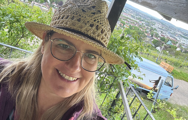 Portrait von Nicole Halte mit einem Strohhut auf der Terrasse von einem Weinberghäusle. Im Hintergrund eine Ape und die Kulisse von Heilbronn. | © DieWeinschmeckerin Nicole Halter