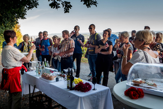 Eine Frau erklärt vor einen Tisch einer Gruppe einen Wein | © Touristikgemeinschaft Hohenlohe e. V.