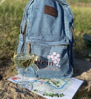 auf einem Stein liegt eine Karte mit einem Weinglas darauf und ein Jeansrucksack | © Nicole Halter