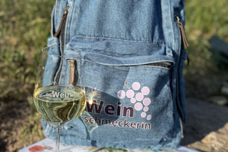 auf einem Stein liegt eine Karte mit einem Weinglas darauf und ein Jeansrucksack | © Nicole Halter
