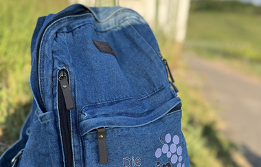 im Vordergrund ein Jeansrucksack mit Weinschmeckerin bestickt, im Hintergrund ein Wengertshäusle | © Nicole Halter