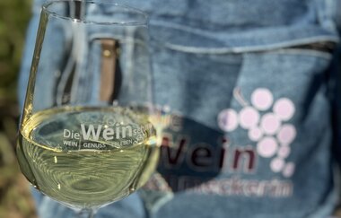 Weinglas mit Weißwein, im Hintergrund ein Jeansrucksack, der auf einer Karte steht | © Nicole Halter