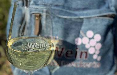 Weinglas mit Weißwein, im Hintergrund ein Jeansrucksack, der auf einer Karte steht | © Nicole Halter