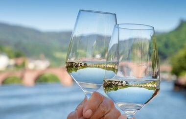 Zwei Gläser, die sich zuprosten. Im Hintergrund die Alte Brücke. | © Heidelberg Marketing GmbH, Foto Tobias Schwerdt