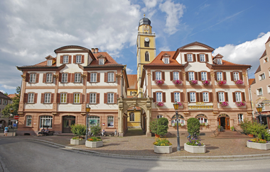 Die Zwillingshäuser sind architektonisch nahezu identisch und durch einen Portalbogen miteinander verbunden. Im Hintergrund sieht man den Turm des Münsters. | © Stadt Bad Mergentheim