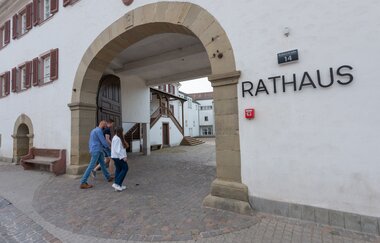 Zwei Menschen laufen durch den steinernen Rundbogen zum Eingang Rathaus Helmstadt | © Stadt Sinsheim