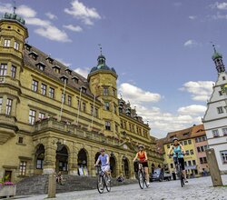 Blick auf den Marktplatz mit Rathaus in Rothenburg o.d.T.  Hier fahren gerade drei Radelnde über das Kopfsteinpflaster.