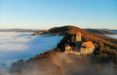 Die Wachenburg thront auf einem Berggrat im Sonnenschein, darunter ist nur Nebel zu sehen. | © Daniel Sieler