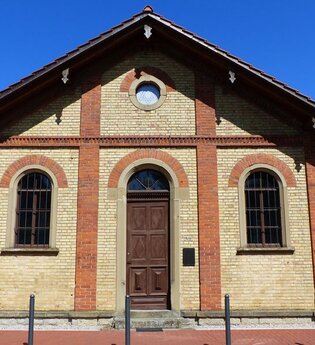 Synagoge aus Backsteinen mit großer Holztüre und zwei Fenstern vor blauem Himmel | © Alte Synagoge Steinsfurt