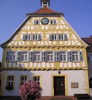 Ein Fachwerkhaus mit gelben Balken, Uhr und steinerner Tafel