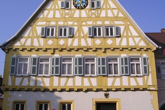 Ein Fachwerkhaus mit gelben Balken, Uhr und steinerner Tafel