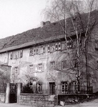 Schwarz-Weiß-Foto eines historischen Gebäudes hinter einer Steinmauer | © Unbekannt