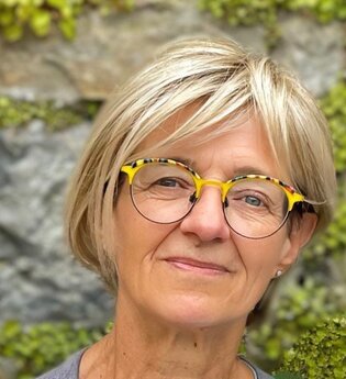 lächenlnde Frau mit blonden Haaren und Brille vor einen begrünten Mauer | © Anja Schué