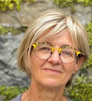 lächenlnde Frau mit blonden Haaren und Brille vor einen begrünten Mauer | © Anja Schué