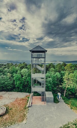 Luftaufnahme vom Aussichtsturm mit Nebengebäude auf dem Stahlberg in Külsheim-Uissigheim. Im Hintergrund geht der Blick ins bewaldete Taubertal.  Der Himmel zeigt ein wildes Wolkenschauspiel in dunkelblau und weiß. | © Liebliches Taubertal