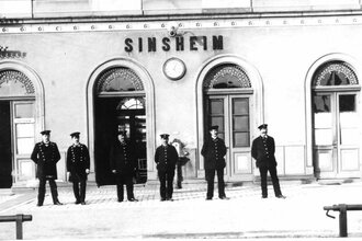 Antikes Schwarz-Weiß-Foto mit Bahnmitarbeitern in Uniformen vor dem Bahnhofsgebäude Sinsheim | © Unbekannt