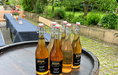 Holzfass mit Cider-Flaschen auf dem Hof, mit einem langen gedeckten Tisch im Hintergrund | © Touristikgemeinschaft Hohenlohe e. V. | Manfred Böhm