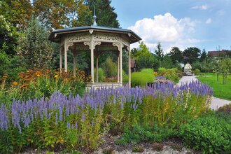 Historischer Pavillon inmitten blühender Stauden unter blauem Himmel.