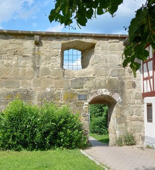 Historische Steinmauer mit kleinem Torbogen und Fachwerkhaus in Gaildorf. | © Petra Natzkowski