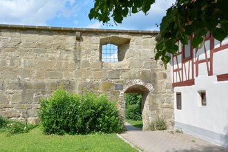 Historische Steinmauer mit kleinem Torbogen und Fachwerkhaus in Gaildorf. | © Petra Natzkowski
