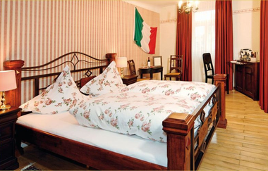 Schlafzimmer mit großem Bett vor gestreifter Tapete und roten Vorhängen | © Unbekannt