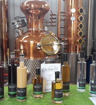 Destillate und Liköre stehen in Flaschen vor einem Brennkessel | © Touristikgemeinschaft Hohenlohe e. V. | Brennerei Weippert