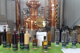 Destillate und Liköre stehen in Flaschen vor einem Brennkessel | © Touristikgemeinschaft Hohenlohe e. V. | Brennerei Weippert