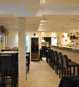 Der helle Innenräume verfügt über schwarze Barhocker an der Wand und um den Tresen | © Touristikgemeinschaft Hohenlohe e. V. | Café de Paris