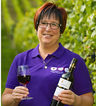 Eine Frau hält eine Flasche Rotwein und ein Glas in der Hand, sie steht in einem Weinberg | © Touristikgemeinschaft Hohenlohe e. V. | Obst- und Weinbau Dietz