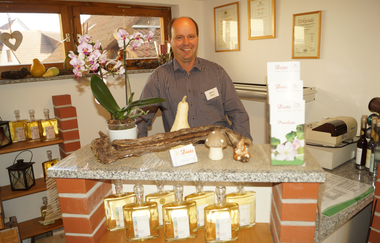 Roland Dietz steht hinter der Verkaufstheke im Hofladen, im Laden sind Regale mit Bränden und Produkten direkt vom Erzeuger | © Touristikgemeinschaft Hohenlohe e.V. | Roland Dietz